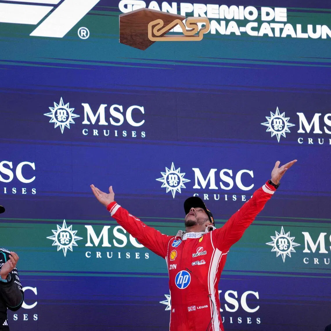 Ferrari's Lewis Hamilton celebrates by tossing his trophy into the air after winning the Barcelona-Catalunya Grand Prix as his former teammate George Russell (left) of Mercedes and McLaren's Lando Norris (right) watch on.