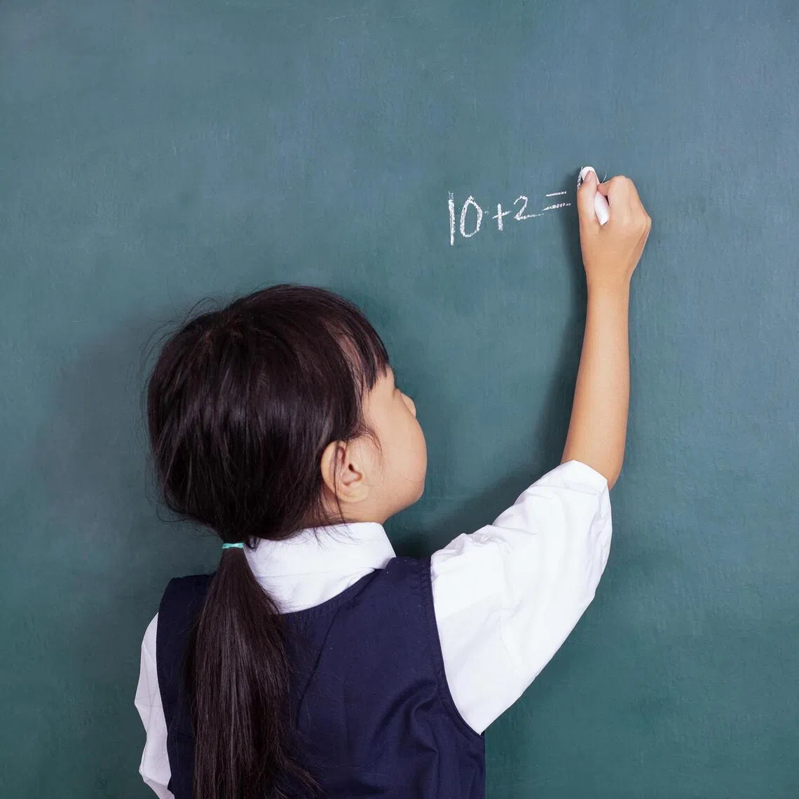 Asian Chinese little girl writing on blackboard in the classroom.