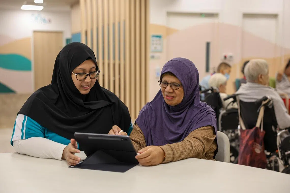 Madam Maria Hadi, who was diagnosed with dementia in 2025, playing a cognitive game at NTUC Health’s Day Centre for Seniors in Kampung Admiralty. With her is NTUC Health staff member Kamaria Md Yassin.