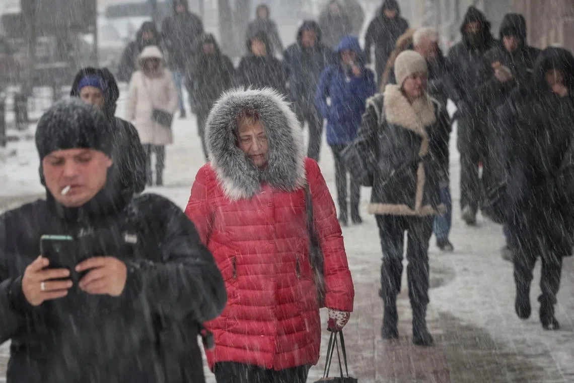 People walk along a street as snow falls, in central Kyiv, on Dec 7, 2022.
