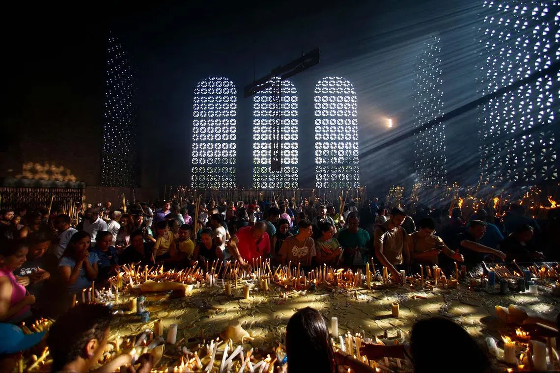 TOPSHOT - Devotees pray next to votive candles while paying tribute to Our Lady of Aparecida, national patroness of Brazil, at the Basilica of the National Shrine in Aparecida, Sao Paulo State, Brazil, on October 12, 2024. (Photo by Miguel SCHINCARIOL / AFP)