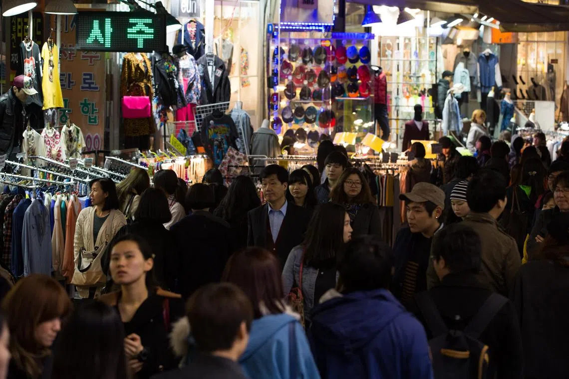 People walk through the Hongdae shopping district at night in Seoul, South Korea, on Saturday, 23 March 2013. South Korea's economy expanded less than previously estimated in the fourth quarter, boosting the case for stimulus by the new government and underscoring concern that a weaker yen will curb exports.  BLOOMBERG
