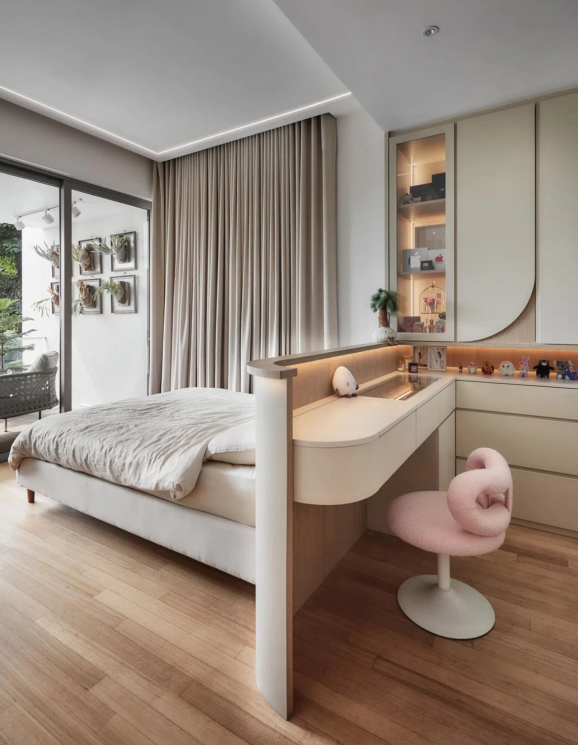 In the master bedroom, a built-in dresser and soft wood tones create an intimate atmosphere. The wife’s pink boucle chair adds a feminine touch.