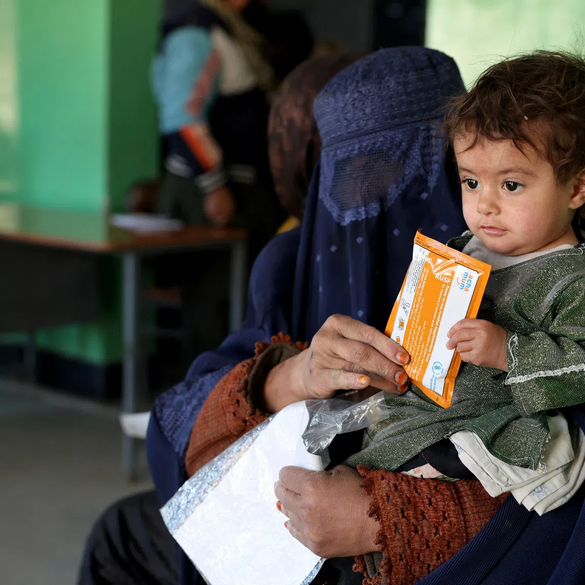 Halima, 40, holds her child with a sachet of Plumpy’Nut, while sitting on a bench at the WFP-supported Qasaba Clinic after an increase in malnutrition cases following the return of deported Afghans, in Kabul, Afghanistan, January 7, 2026. REUTERS/Sayed Hassib
