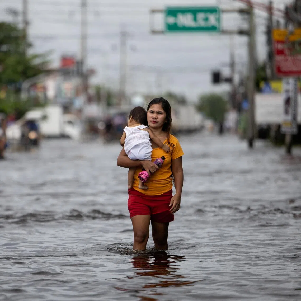 A woman carrying a baby wades through a flooded area in Manila North Road following heavy rains brought by Typhoon Co-may in Minalin, Pampanga, Philippines, July 25, 2025. REUTERS/Eloisa Lopez