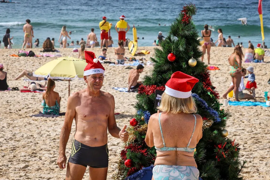 A beachgoer posing for a photo in front of a Christmas tree on Christmas Day at Bondi Beach in Sydney on Dec 25, 2023.