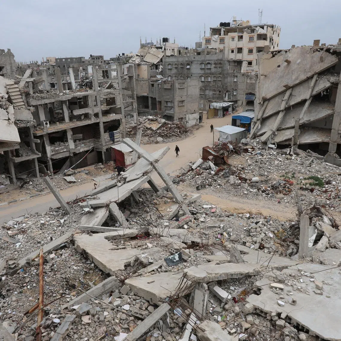 Palestinians walk surrounded by the rubble of houses destroyed in Israeli strikes during the war, in Khan Younis, southern Gaza Strip, January 22, 2026. REUTERS/Ramadan Abed
