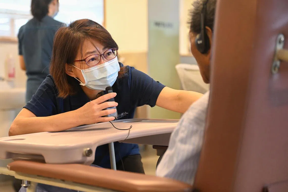 Advanced practice nurse Jessie Tan from Yishun Health, speaks to her patient Mr Gan Chwee Tin, 85, via a hearing aid at a ward in Yishun Community Hospital.  She is one of nearly 400 staff at Yishun Health trained in Humanitude, a new care practice that empowers seniors and caregivers.

