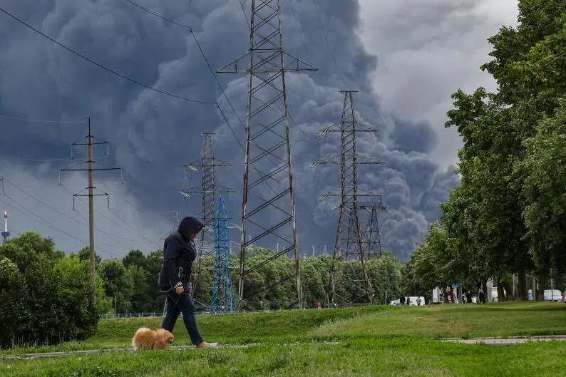 A woman walking in a park as smoke billows in the background following a reported Ukrainian drone attack, in Moscow, Russia, on June 18.