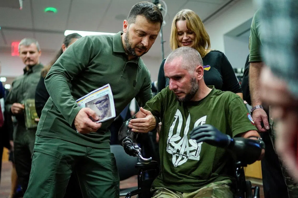 Mr Zelensky helps a wounded soldier to stand up as he gives him an award during his visit at the Staten Island University Hospital.