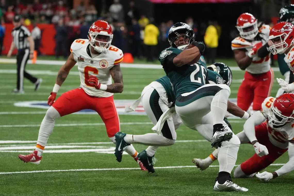 Philadelphia Eagles' running back Saquon Barkley (N0. 26) rushes with the football as he is pursued by Kansas City Chiefs' safety Bryan Cook (left) and Kansas City Chiefs' linebacker Joshua Uche during Super Bowl LIX.