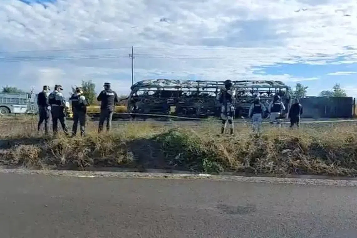 A still image from video shows security forces standing near a charred vehicle, following the highway collision between a truck and a bus filled with passengers, in Mexico.