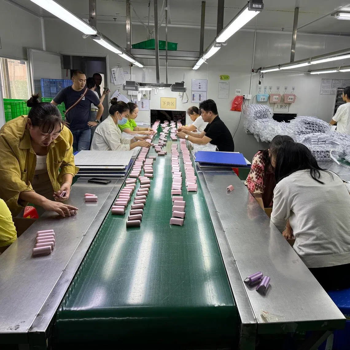 Vape shells waiting to be spray-painted and inspected by a row of workers in a small workshop in Shenzhen.