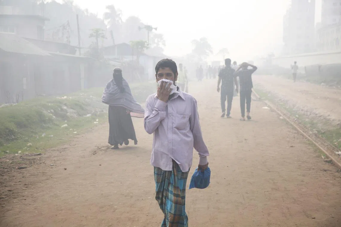 A man covers his mouth and nose as he walks along an area surrounded by smoke and dust in Shampur, Dhaka, on Feb 23, 2023. 