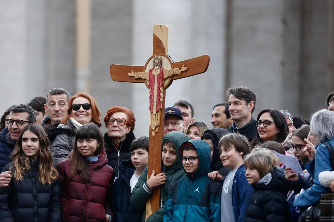 Pilgrims pose with a wooden cross at St Peter's Square at the Vatican.