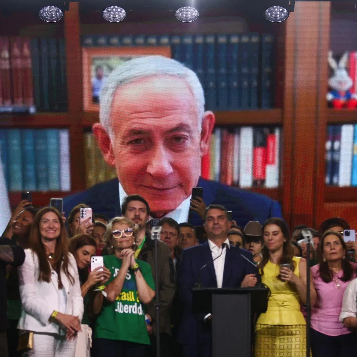 Brazilian Senator Flavio Bolsonaro, who is to be announced as candidate for Brazil's presidential elections, stands in front of a screen showing a pre-recorded message from Israeli Prime Minister Benjamin Netanyahu during the national convention of the Liberal Party (PL) in Sao Paulo, Brazil, July 25, 2026. REUTERS/Jean Carniel