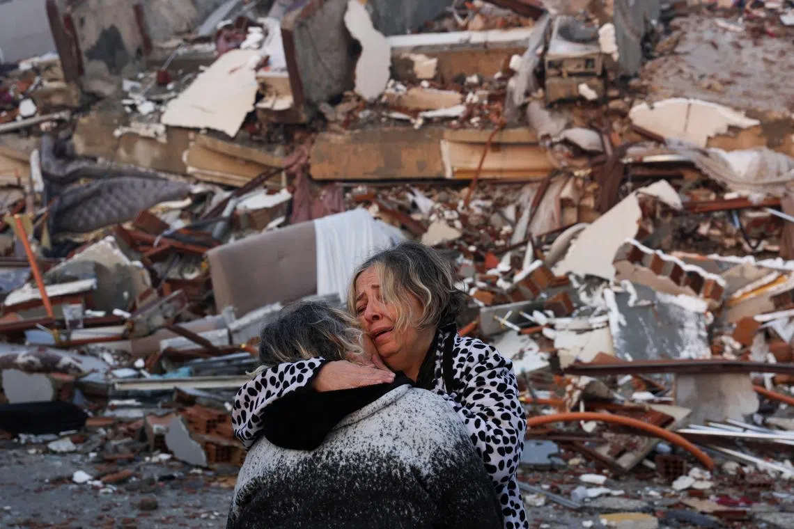 A woman reacts while embracing another person, near rubble following an earthquake in Hatay, Turkey, Feb 7, 2023. 