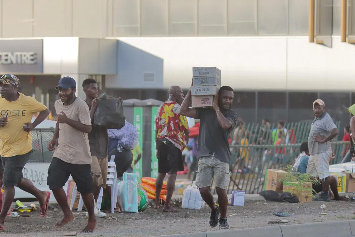 People carry looted goods amid a state of unrest in Port Moresby on Jan 10 during protests over a pay cut for Papua New Guinean police and public sector employees.