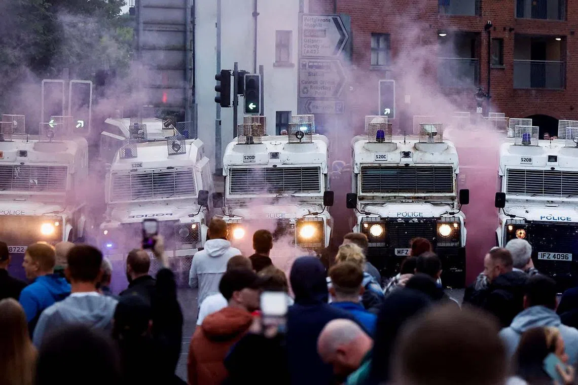 Coloured smoke billowing as demonstrators gather in front of riot police vehicles as riots continue in Ballymena, Northern Ireland, June 11, 2025. 