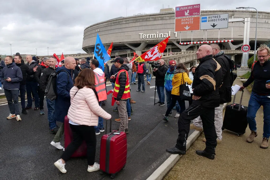 Passengers walk on the road with their luggages as airport workers on strike gather outside the Terminal 1.