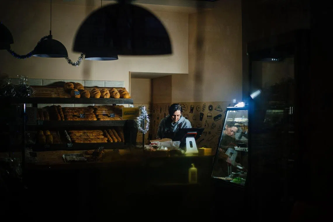 TOPSHOT - A woman sells bread using LED lighting during a blackout after a Russian missile attack in the southern city of Mykolayiv on December 31, 2022. - Russian strikes on December 31, targeted several regions of Ukraine, including the capital Kyiv, where the attacks killed at least one person and wounded several others, Ukrainian officials said. (Photo by Dimitar DILKOFF / AFP)