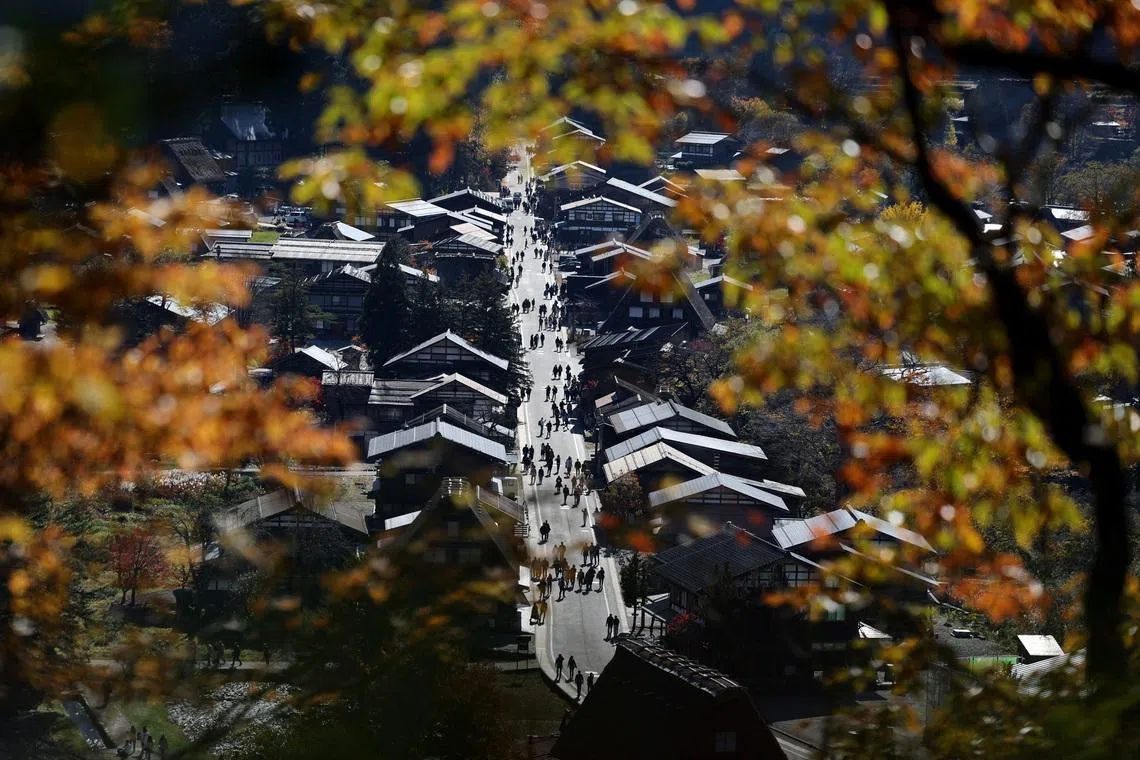 Visitors strolling next to traditional Gassho-style houses are seen through autumn-colored leaves at Shirakawa-go, a popular tourist spot and one of Japan's UNESCO World Heritage sites, in Shirakawa village, Gifu Prefecture, Japan, November 15, 2025. REUTERS/Issei Kato
