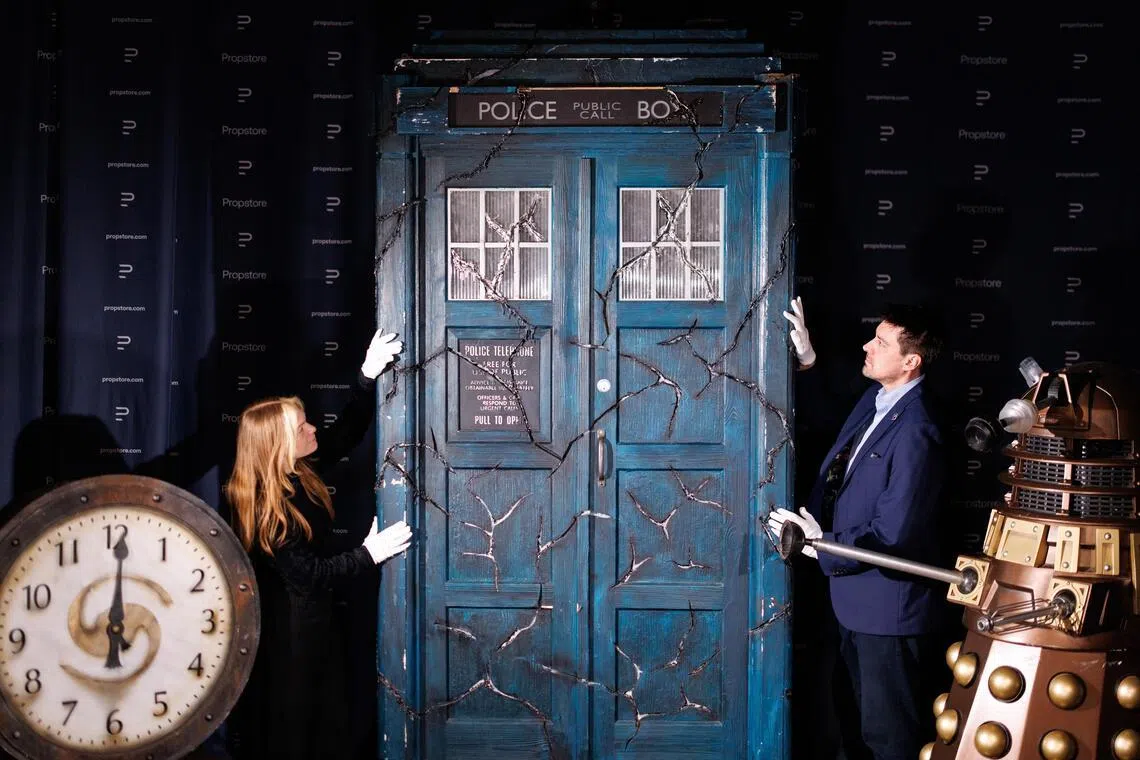 Propstore employees pose with a screen-matched TARDIS (middle), a Bronze Asylum Dalek (right and a Sardickton Clock (left), which were used in the filming of the TV series Doctor Who.