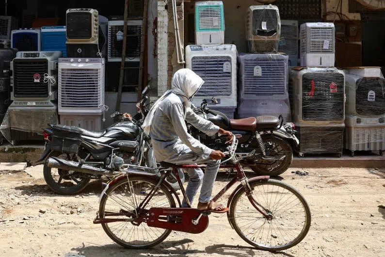 A man with his face covered to beat the heat riding past air coolers displayed outside a shop on a hot summer day in Varanasi, India.