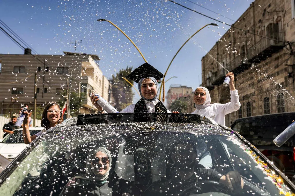 A Palestinian student celebrating in a car as others spray foam around her after the Palestinian Education Ministry announced the results for high school diploma examinations, in the city of Hebron in the occupied West Bank on July 20, 2023.