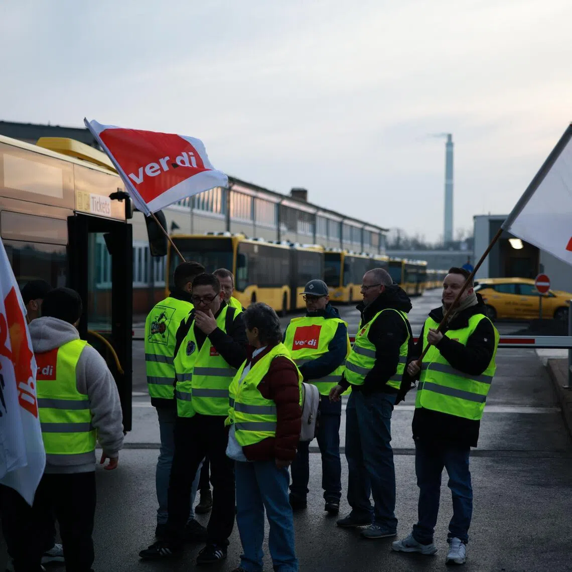 Employees with flags stand in front of parked buses at the BVG bus depot Lichtenberg during a public transport warning strike in Berlin, Germany, on Feb 27, 2026.