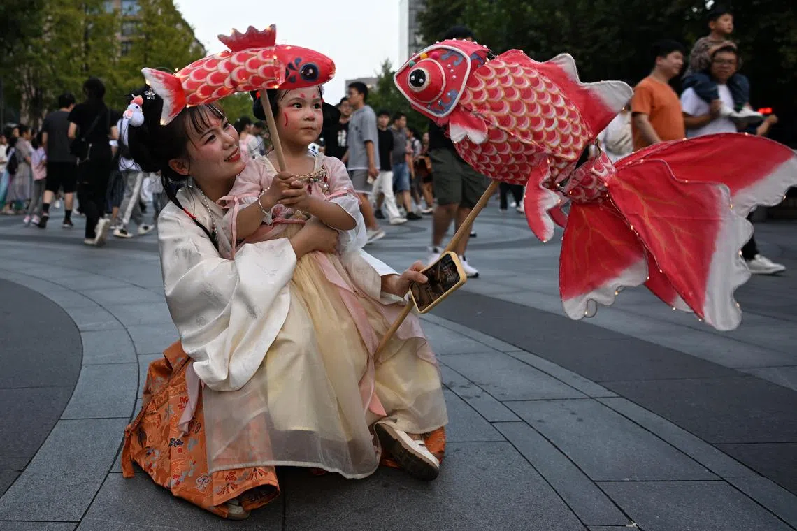 Chen Hongmei and her daughter Liu Yiyi, holding lanterns made from recycled material and dressed in traditional costume, celebrating the Mid-Autumn Festival at West Lake in Hangzhou on Friday.