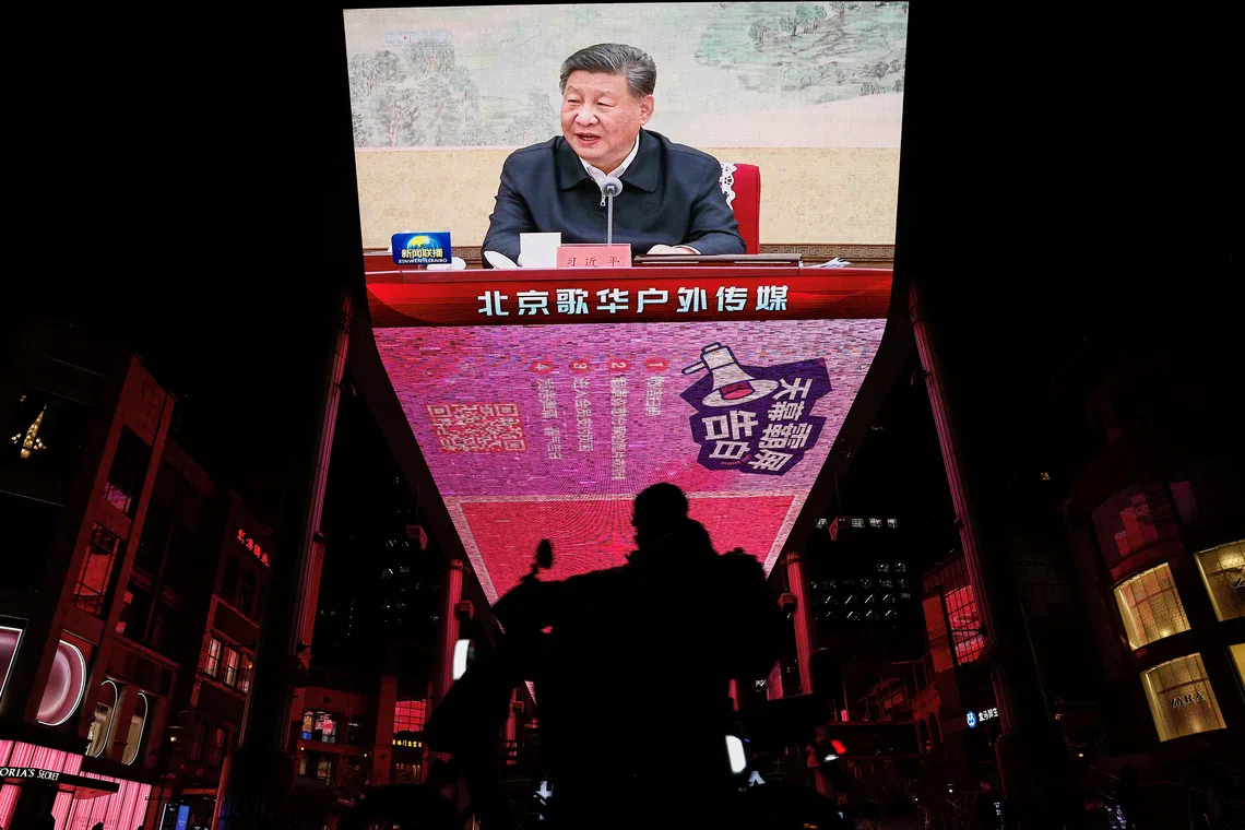A man rides a scooter past a giant screen showing news footage of Chinese President Xi Jinping attending a Chinese Communist Party politburo meeting, in Beijing, China December 9, 2024. REUTERS/Tingshu Wang