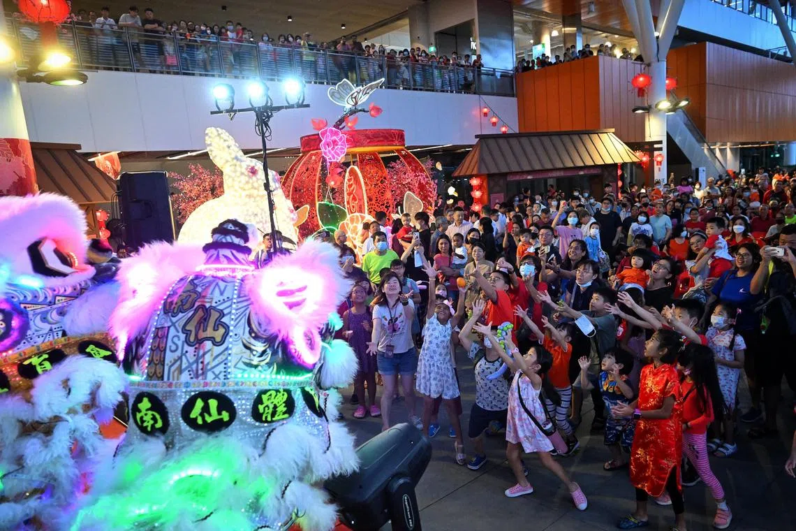 Residents reaching for oranges tossed out during the lion dance performance as One Punggol hosted its Chinese New Year celebrations at the integrated community hub on Jan 20, 2023.