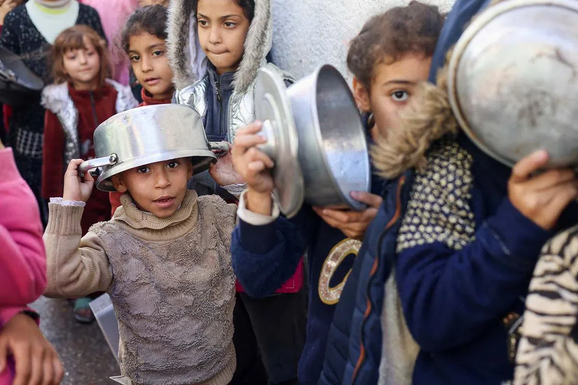 Palestinian children carrying pots as they queue to receive food cooked by a charity kitchen, amid shortages in food supplies, as the conflict between Israel and Hamas continues, in Rafah in the southern Gaza Strip, Dec 14, 2023. 