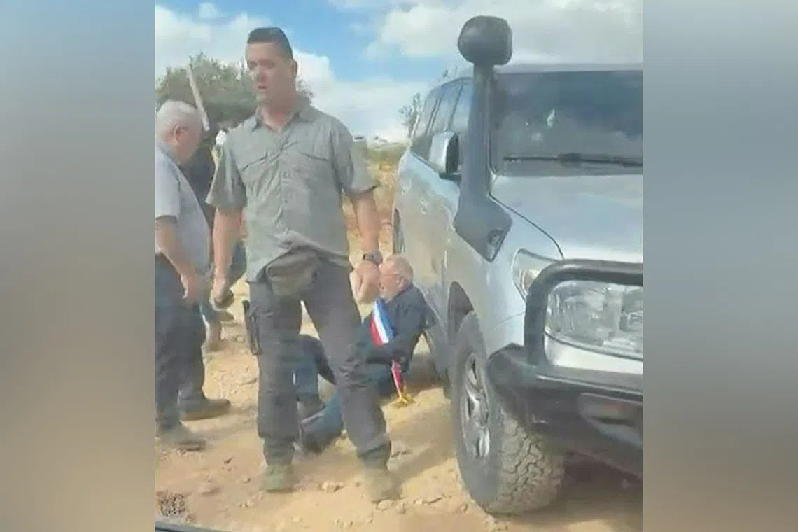 A man wearing a blue, white and red sash, of the type used by French public officials, leaning against a vehicle as men intercept and surround a car carrying activists in the Christian village of Taybeh, in the Israeli-occupied West Bank.