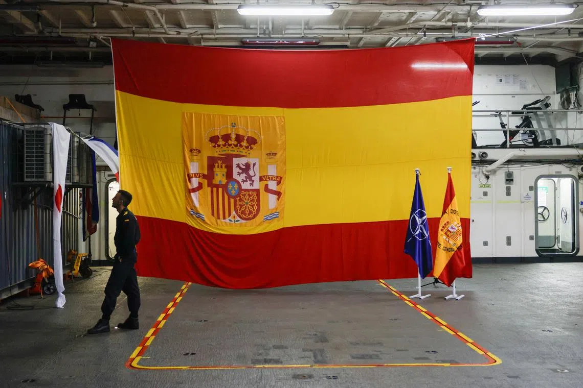 A Spanish Navy soldier stands next to Spanish flags and a NATO flag at the hangar of the Castilla LPD (Landing Platform Dock) type amphibious assault ship during a naval parade.