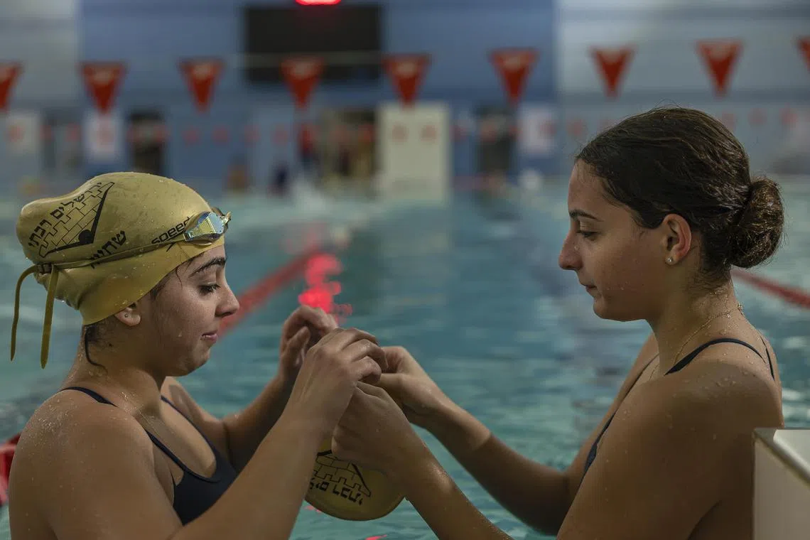 Shira Chuna, left, and Avishag Ozeri, swimmers with the Greater Jerusalem swim club, whose membership is mixed Israeli and Palestinian, help one another with their gear at a YMCA pool in Jerusalem on Nov. 5, 2023. The rule was unspoken, but long abided: No politics in the pool. The October 7 attacks, and the Israel bombardment of Gaza that followed, has sorely tested it. (Afif H. Amireh/The New York Times)



