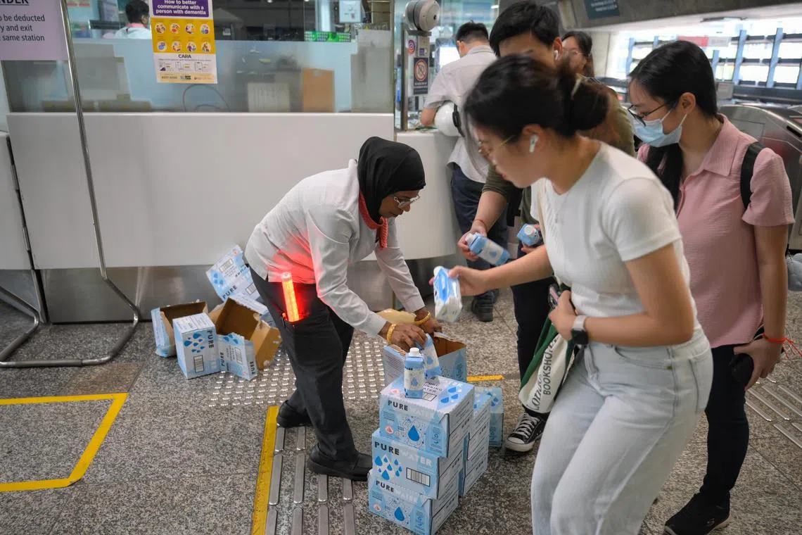 An SMRT employee giving out water to commuters as she directs them to the bridging bus service at Clementi MRT station after a train fault between Boon Lay and Queenstown, on Sept 25, 2024.