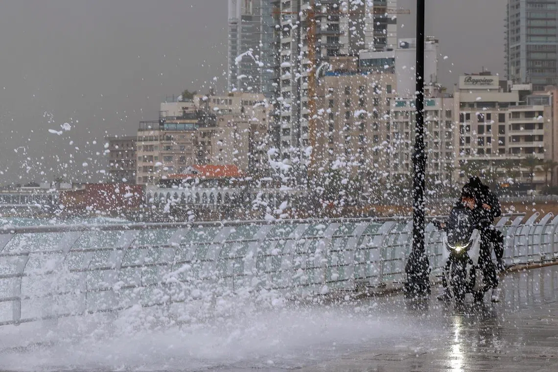 Two men on a motorcycle riding past a high-rising wave on the Corniche Al Manara in Beirut, Lebanon, Jan 12, 2026. 