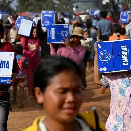 Displaced people carry boxes with drinking water distributed at a temporary camp in Cambodia's Oddar Meanchey province on December 11, 2025.
