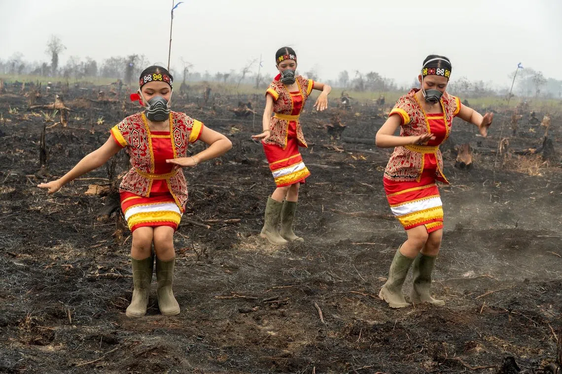 Members of Zwageri Generation performing a traditional Dayak dance while wearing gas masks and rubber boots on burnt out peatland in Ketapang, West Kalimantan.