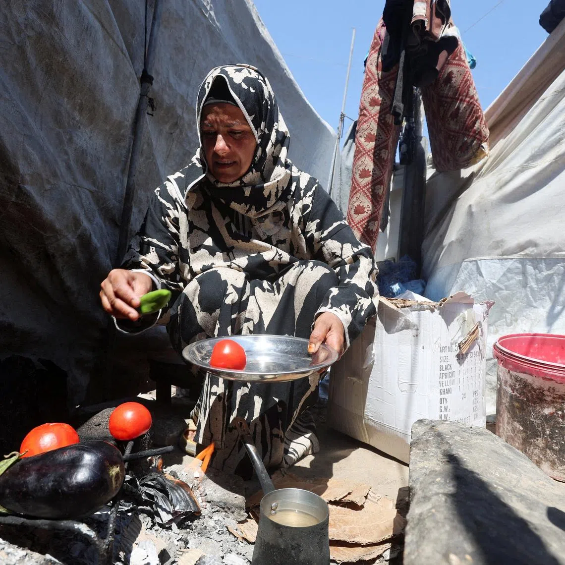 Displaced Palestinian woman Nisreen Abu Saada cook vegetables over a wood fire outside her tent, amid shortages of lighters and cooking gas, in Khan Younis, in the southern Gaza Strip, July 21, 2026. REUTERS/Ramadan Abed