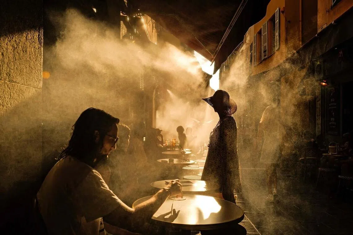 TOPSHOT - People stand in front of a coffe shop during a heatwave in the French Riviera city of Nice on July 6, 2026. (Photo by Valery HACHE / AFP)