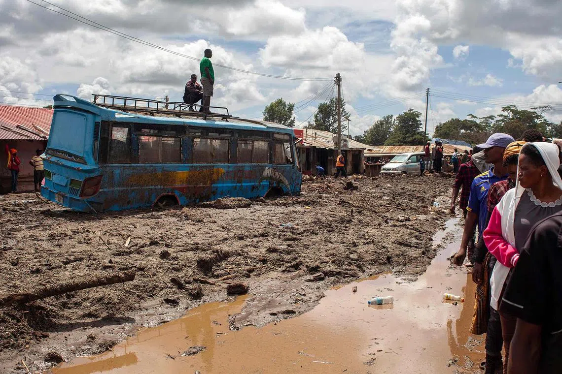 TOPSHOT - Two men stand on top of a bus as others gather to assess damages at a street covered on mud following landslides and flooding triggered by heavy rainfall in Katesh, Tanzania on December 5, 2023. Torrential downpours in northern Tanzania washed away vehicles and brought down buildings in the hillside town of Katesh, 300 kilometres (185 miles) north of the capital Dodoma. The death toll from landslides and flooding triggered by heavy rainfall in northern Tanzania climbed to 68 on December 4, a regional official said, as rescue workers searched for trapped survivors. (Photo by Ebby SHABAN / AFP)