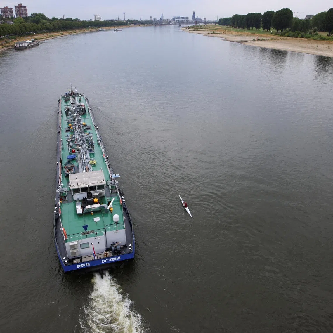 A canoer paddles next to a cargo ship at low water levels in the Rhine river in Cologne, Germany, August 15, 2022. REUTERS/Thilo Schmuelgen