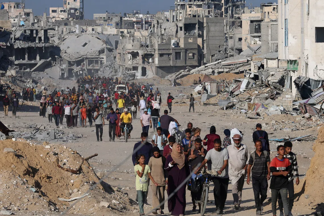 Palestinians walk past rubble as they return to their neighborhood, following Israeli forces' withdrawal from the area, amid a ceasefire between Israel and Hamas in Gaza, in Khan Younis, in the southern Gaza Strip October 11, 2025. REUTERS/Ramadan Abed