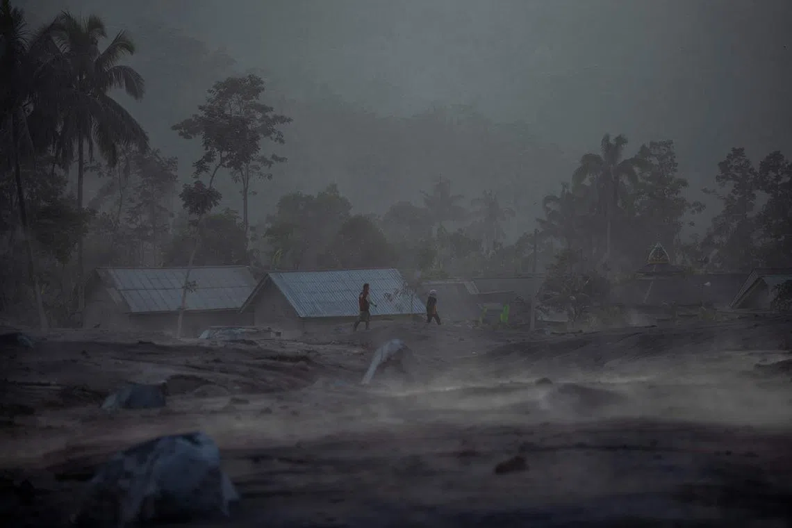 People walk past houses following a volcanic eruption by Mount Semeru at Kajar Kuning village in Lumajang on Dec 5, 2022. 