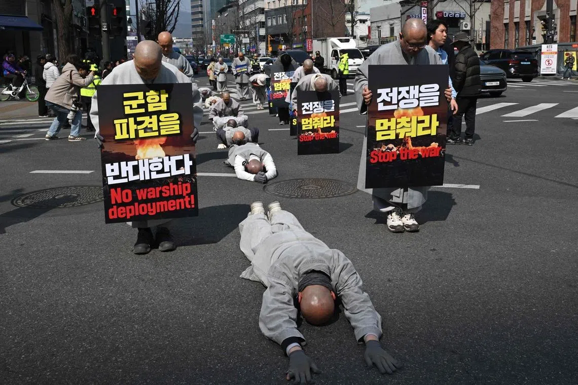 TOPSHOT - South Korean Buddhist monks perform full bows as they march towards the US embassy during a protest against the war on Iran in Seoul on March 17, 2026. (Photo by Jung Yeon-je / AFP)