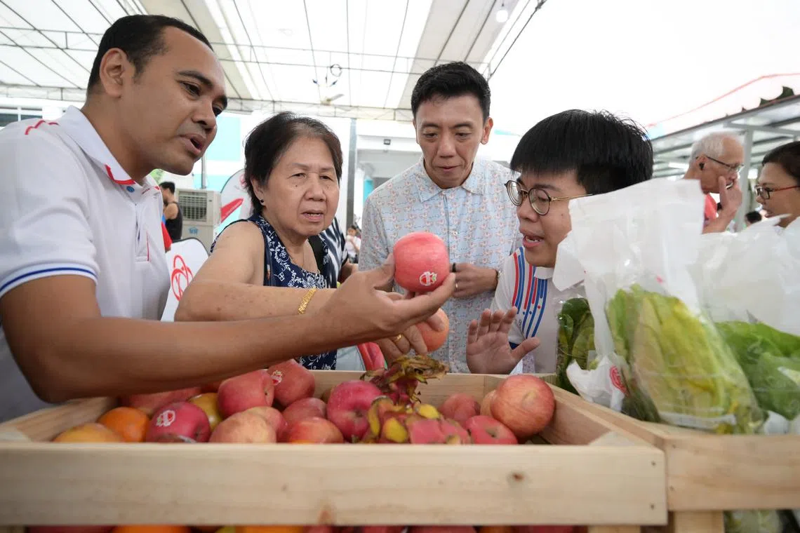 Chua Chu Kang GRC MPs Mr Zhulkarnain Abdul Rahim (left) and Mr Jeffrey Siow (second from right) choosing apples with a resident at Brickland Green Festival 2025 on May 17.