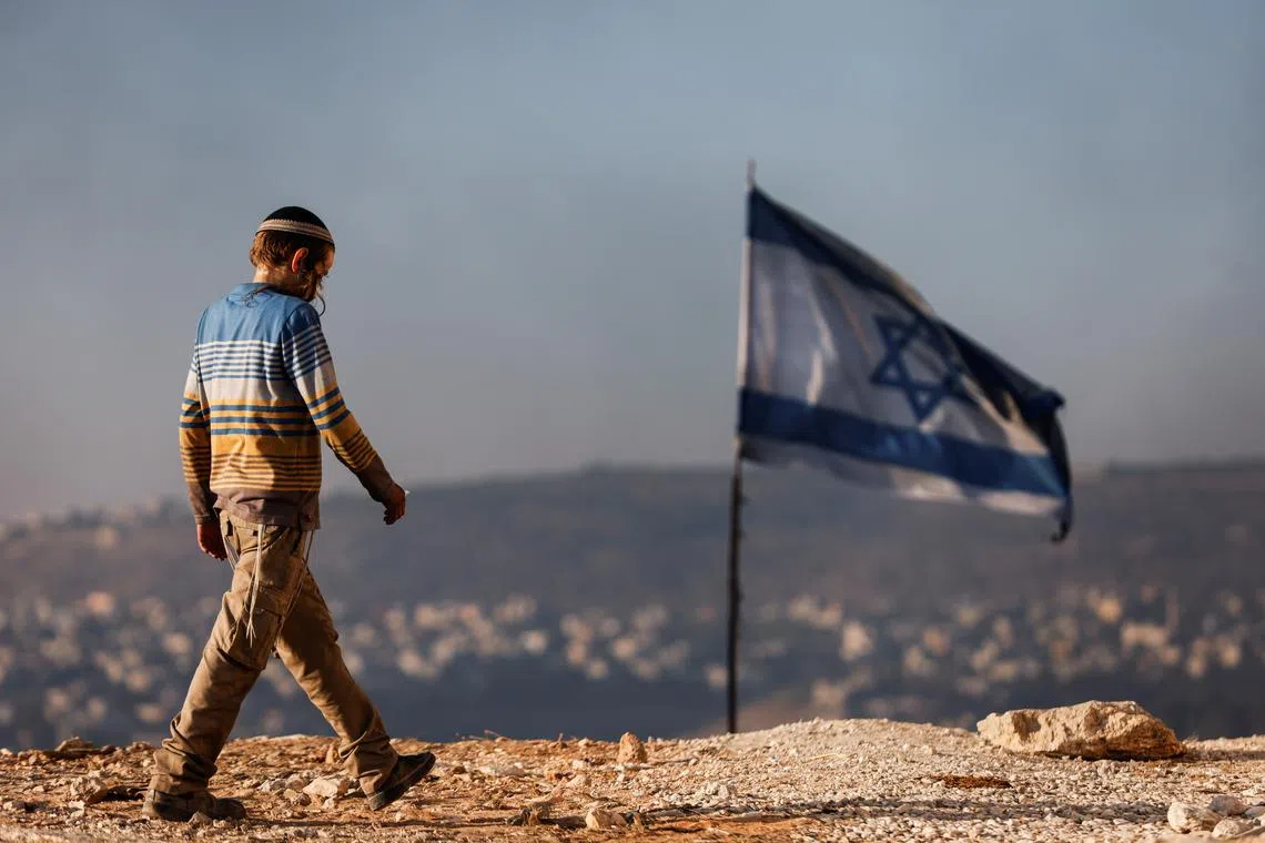 FILE PHOTO: A Jewish settler teenager walks by an Israeli flag in Givat Eviatar, a new Israeli settler outpost, near the Palestinian village of Beita in the Israeli-occupied West Bank June 23, 2021. Picture taken June 23, 2021. REUTERS/Amir Cohen/File Photo
